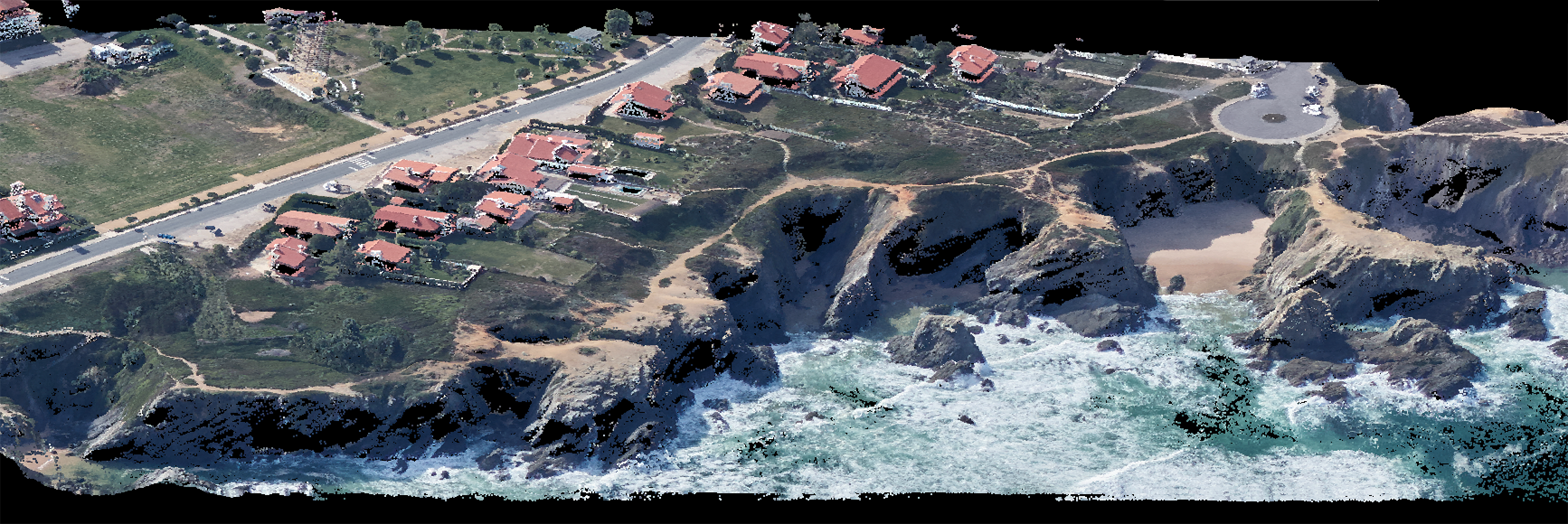 Vue aérienne du littoral de La Réunion, avec les vagues s'écrasant contre des falaises abruptes. Des maisons aux toits rouges parsèment le paysage à gauche, le long d'une route sinueuse. La verdure et le relief rocheux de l'île se marient harmonieusement, avec une petite plage nichée entre les falaises.